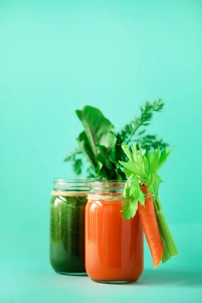 Здоровые органические зеленые и оранжевые коктейли на голубом фоне. Детоксикационные напитки в стеклянной банке из овощей - морковь, сельдерей, свекловичная зелень и топы. Принято. Концепция летней еды — стоковое фото