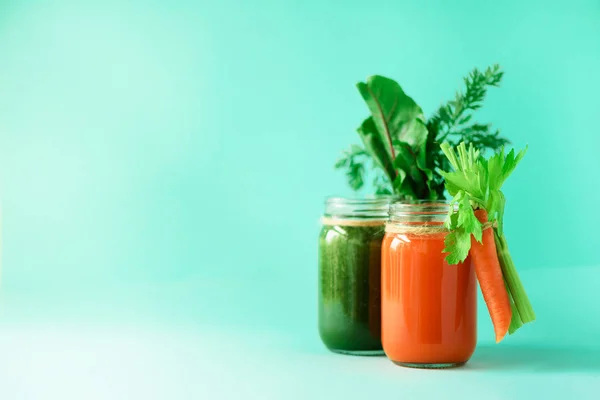 Gezonde biologische groene en oranje smoothies op blauwe achtergrond. Detox drankjes in glazen pot van groenten - wortel, BLEEKSELDERIJ, bieten Groenen en topjes. Kopieer ruimte. Zomer voedsel concept — Stockfoto