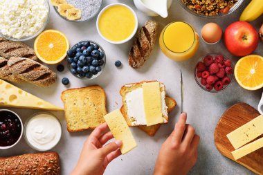 Erkek Yayilim tereyağı ekmek üzerinde eller. Kadın yemek kahvaltı. Sağlıklı kahvaltı maddeler, gıda çerçeve. Granola, yumurta, fındık, meyve, çilek, süt, yoğurt, meyve suyu, peynir. Üstten görünüm, kopya alanı