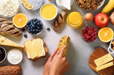 Erkek Yayilim tereyağı ekmek üzerinde eller. Kadın yemek kahvaltı. Sağlıklı kahvaltı maddeler, gıda çerçeve. Granola, yumurta, fındık, meyve, çilek, süt, yoğurt, meyve suyu, peynir. Üstten görünüm, kopya alanı