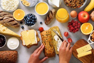 Erkek Yayilim tereyağı ekmek üzerinde eller. Kadın yemek kahvaltı. Sağlıklı kahvaltı maddeler, gıda çerçeve. Granola, yumurta, fındık, meyve, çilek, süt, yoğurt, meyve suyu, peynir. Üstten görünüm, kopya alanı