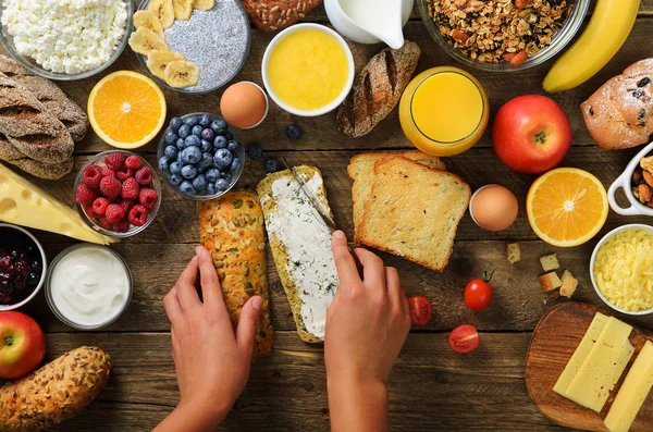 Erkek Yayilim tereyağı ekmek üzerinde eller. Kadın yemek kahvaltı. Sağlıklı kahvaltı maddeler, gıda çerçeve. Granola, yumurta, fındık, meyve, çilek, süt, yoğurt, meyve suyu, peynir. Üstten görünüm, kopya alanı