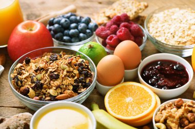 Sağlıklı kahvaltı maddeler, gıda çerçeve. Granola, yumurta, fındık, meyve, çilek, kızarmış ekmek, süt, yoğurt, portakal suyu, peynir, muz, elma ahşap rustik arka plan, üstten görünüm, kopya alanı.