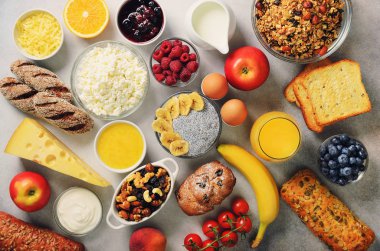 Sağlıklı kahvaltı maddeler, gıda çerçeve. Granola, yumurta, fındık, meyve, çilek, kızarmış ekmek, süt, yoğurt, portakal suyu, peynir, muz, elma gri arka plan, üstten görünüm, kopya alanı.
