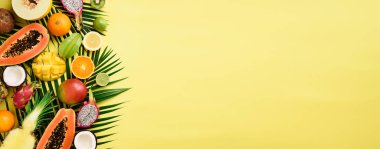 Egzotik meyve ve tropikal palmiye yaprakları üzerinde pastel sarı arka plan - papaya, mango, ananas, muz, carambola, dragon meyve, kivi, limon, portakal, kavun, Hindistan cevizi, kireç. Afiş. Üstten görünüm.