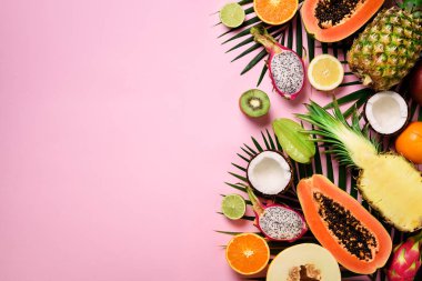 Egzotik meyve ve tropikal palmiye yaprakları üzerinde pastel pembe arka plan - papaya, mango, ananas, muz, carambola, dragon meyve, kivi, limon, portakal, kavun, Hindistan cevizi, kireç. Üstten görünüm.
