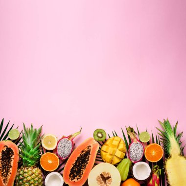 Egzotik meyve ve tropikal palmiye yaprakları üzerinde pastel pembe arka plan - papaya, mango, ananas, muz, carambola, dragon meyve, kivi, limon, portakal, kavun, Hindistan cevizi, kireç. Üstten görünüm.