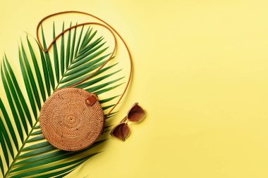 Yuvarlak rattan çanta, sarı zemin üzerine güneş gözlüğü. Afiş. Üstten görünüm kopya alanı ile. Trendy bambu çanta ve beyaz ayakkabı. Yaz moda düz yatıyordu. Gezi, tatil kavramı