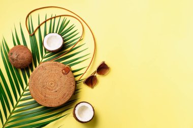Rattan çanta, Hindistan cevizi, birkenstocks, hurma dalları güneş gözlüğü üzerinde arka plan sarı. Afiş. Üstten görünüm kopya alanı ile. Trendy bambu çanta ve ayakkabılar. Yaz moda düz yatıyordu. Gezi, tatil kavramı
