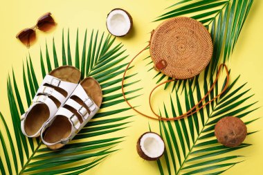 Rattan çanta, Hindistan cevizi, birkenstocks, hurma dalları güneş gözlüğü üzerinde arka plan sarı. Afiş. Üstten görünüm kopya alanı ile. Trendy bambu çanta ve ayakkabılar. Yaz moda düz yatıyordu. Gezi, tatil kavramı