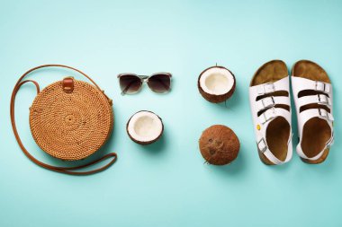 Şık rattan çanta, Hindistan cevizi, birkenstocks, hurma dalları, mavi arka plan üzerinde güneş gözlüğü. Afiş. Üstten görünüm kopya alanı ile. Trendy bambu çanta ve beyaz ayakkabı. Yaz moda düz yatıyordu