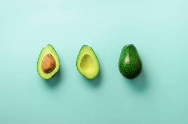 Organik avokado tohumu, avokado yarısı ve mavi arka plan üzerinde tüm meyve ile. Üstten görünüm. Pop sanat tasarım, yaratıcı yaz gıda kavramı. Yeşil avocadoes desen en az daire yatıyordu tarzı.
