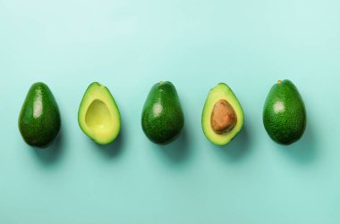 Organik avokado tohumu, avokado yarısı ve mavi arka plan üzerinde tüm meyve ile. Üstten görünüm. Pop sanat tasarım, yaratıcı yaz gıda kavramı. Yeşil avocadoes desen en az daire yatıyordu tarzı.