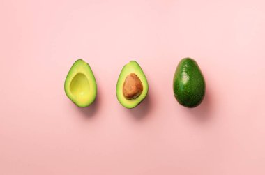 Organik avokado tohumu, avokado yarısı ve pembe bir arka plan üzerinde tüm meyve ile. Üstten görünüm. Pop sanat tasarım, yaratıcı yaz gıda kavramı. Yeşil avocadoes desen en az daire yatıyordu tarzı.