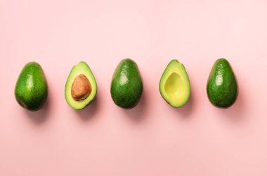 Organik avokado tohumu, avokado yarısı ve pembe bir arka plan üzerinde tüm meyve ile. Üstten görünüm. Pop sanat tasarım, yaratıcı yaz gıda kavramı. Yeşil avocadoes desen en az daire yatıyordu tarzı.
