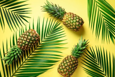 Ananas ve tropikal palmiye yaprakları sarı arka plan üzerinde. Üstten görünüm. Yaz konsepti. Yaratıcı düz lay kopya alanı ile.