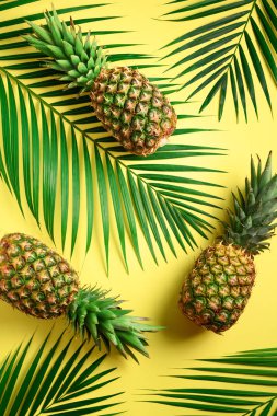 Ananas ve tropikal palmiye yaprakları sarı arka plan üzerinde. Üstten görünüm. Yaz konsepti. Yaratıcı düz lay kopya alanı ile.