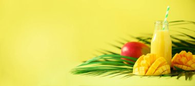 Turuncu meyve ve sarı zemin üzerine mango ile lezzetli sulu güler yüzlü. Uzay kopyalayın. Pop sanat tasarım, yaratıcı yaz konsepti. Yeşil palmiye üzerinde cam şişelerde taze meyve suyu bırakır. Afiş