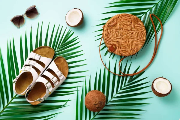 Bolsa de ratán redonda, coco, birkenstocks, ramas de palma, gafas de sol sobre fondo azul. Banner. Vista superior con espacio de copia. Bolso y zapatos de bambú de moda. Verano de moda plana laico. Viaje, concepto de vacaciones — Foto de Stock