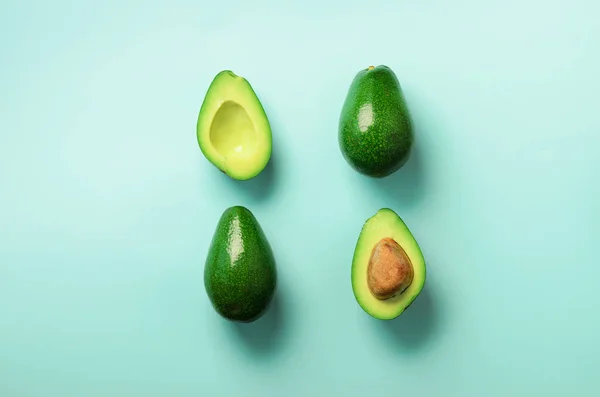 Organik avokado tohumu, avokado yarısı ve mavi arka plan üzerinde tüm meyve ile. Üstten görünüm. Pop sanat tasarım, yaratıcı yaz gıda kavramı. Yeşil avocadoes desen en az daire yatıyordu tarzı. — Stok fotoğraf