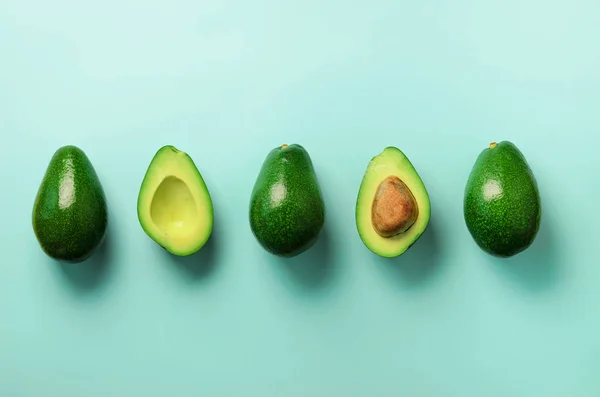 Органический авокадо с семенами, половинками авокадо и цельными фруктами на голубом фоне. Вид сверху. Поп-арт дизайн, креативная концепция летней еды. Зеленый авокадо рисунок в минимальном стиле . — стоковое фото