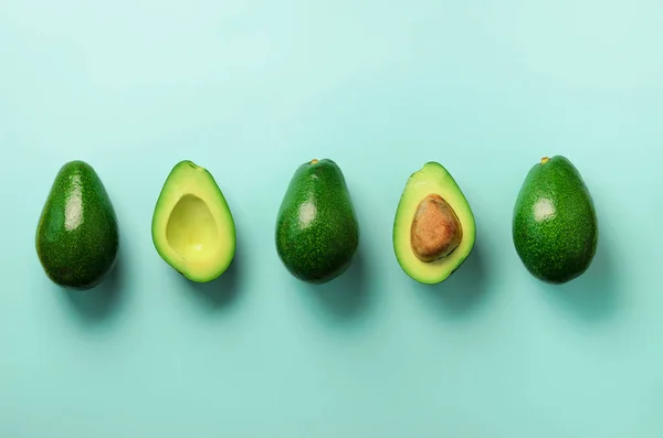 Aguacate ecológico con semillas, mitades de aguacate y frutas enteras sobre fondo azul. Vista superior. Diseño de arte pop, concepto creativo de comida de verano. Patrón de aguacates verdes en estilo laico plano mínimo . — Foto de Stock