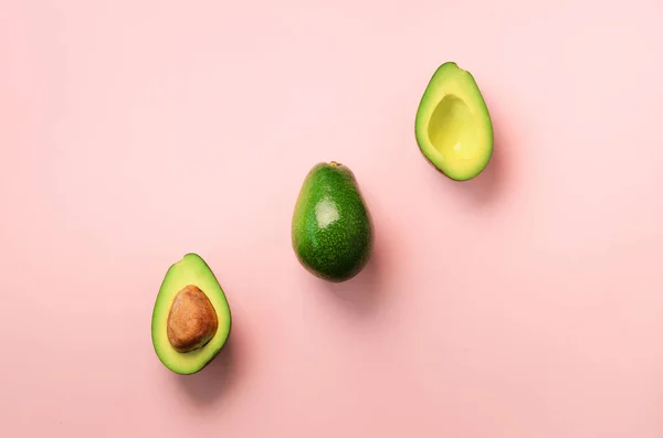 Aguacate ecológico con semillas, mitades de aguacate y frutas enteras sobre fondo rosa. Vista superior. Diseño de arte pop, concepto creativo de comida de verano. Patrón de aguacates verdes en estilo laico plano mínimo . — Foto de Stock