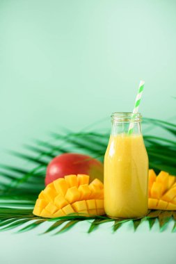 Turuncu meyve ve turkuaz arka plan üzerinde mango ile lezzetli sulu güler yüzlü. Uzay kopyalayın. Pop sanat tasarım, yaratıcı yaz konsepti. Yeşil palmiye üzerinde cam şişelerde taze meyve suyu bırakır.