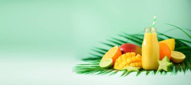 Turuncu meyve ve turkuaz arka plan üzerinde mango ile lezzetli sulu güler yüzlü. Uzay kopyalayın. Pop sanat tasarım, yaratıcı yaz konsepti. Yeşil palmiye üzerinde cam şişelerde taze meyve suyu bırakır. Afiş