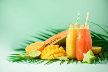 Sulu papaya ve ananas, mango, turuncu meyve yüzlü turkuaz arka plan üzerinde iki kavanoz. , Yaz diyet gıda, vegan kavramı detoks. Uzay kopyalayın. Yeşil palmiye üzerinde cam şişelerde taze meyve suyu bırakır.