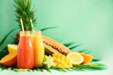 Sulu papaya ve ananas, mango, turuncu meyve yüzlü turkuaz arka plan üzerinde iki kavanoz. , Yaz diyet gıda, vegan kavramı detoks. Uzay kopyalayın. Yeşil palmiye üzerinde cam şişelerde taze meyve suyu bırakır.