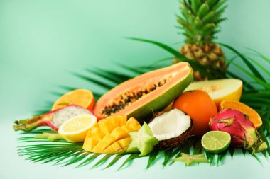 Turkuaz arka plan üzerinde egzotik meyve ürün yelpazesine. Detoks, vegan gıda, yaz konsepti. Papaya, mango, ananas, carambola, dragon meyve, kivi, portakal, kavun, Hindistan cevizi, kireç palmiye yaprakları üzerinde.