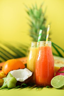 Sulu papaya ve ananas, mango, turuncu meyve yüzlü sarı zemin üzerine iki kavanoz. , Yaz diyet gıda, vegan kavramı detoks. Uzay kopyalayın. Yeşil palmiye üzerinde cam şişelerde taze meyve suyu bırakır.