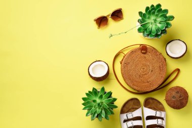 Şık rattan çanta, Hindistan cevizi, birkenstocks, etli, sarı zemin üzerine güneş gözlüğü. Afiş. Üstten görünüm kopya alanı ile. Trendy bambu çanta ve beyaz ayakkabı. Yaz moda düz yatıyordu