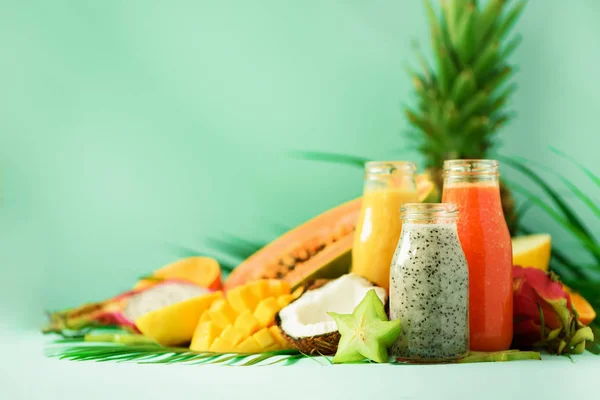 Papaya, dragon fruit, pineapple, mango smoothie in jars on turquoise background. Detox, vegan diet food, healthy eating concept. Banner. Copy space. Fresh juice in glass bottles over palm leaves. — Stock Photo, Image