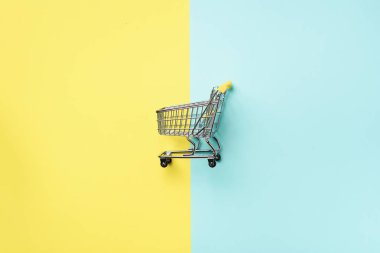 Mavi ve sarı zemin üzerine alışveriş sepeti. Minimalizm tarzı. Yaratıcı tasarım. Üstten görünüm kopya alanı ile. Süpermarkette alışveriş arabası. Satış, iskonto, shopaholism kavramı. Tüketici Derneği eğilim