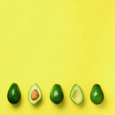 Organik avokado tohumu, avokado yarısı ve sarı zemin üzerine tüm meyve ile. Üstten görünüm. Kare ürün. Pop sanat tasarım, yaratıcı yaz gıda kavramı. Yeşil avocadoes desen en az daire yatıyordu tarzı.