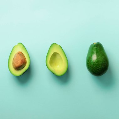 Organik avokado tohumu, avokado yarısı ve mavi arka plan üzerinde tüm meyve ile. Üstten görünüm. Pop sanat tasarım, yaratıcı yaz gıda kavramı. Yeşil avocadoes desen en az daire yatıyordu tarzı. Kare kırpma