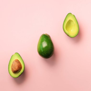Organik avokado tohumu, avokado yarısı ve pembe bir arka plan üzerinde tüm meyve ile. Üstten görünüm. Kare ürün. Pop sanat tasarım, yaratıcı yaz gıda kavramı. Yeşil avocadoes desen en az daire yatıyordu tarzı.