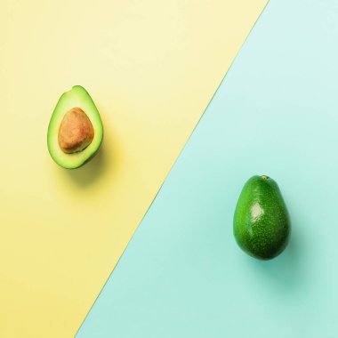 Avokado tohum, meyve mavi ve sarı zemin üzerine dilimlenmiş. Üstten görünüm. Pop sanat tasarım, yaratıcı yaz gıda kavramı. En az düz stil yatıyordu. Kare kırpma