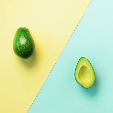 Avokado tohum, meyve mavi ve sarı zemin üzerine dilimlenmiş. Üstten görünüm. Pop sanat tasarım, yaratıcı yaz gıda kavramı. En az düz stil yatıyordu. Kare kırpma.