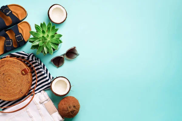 Kadın birkenstock sandalet, kot, tişört, rattan çanta, Hindistan cevizi ve güneş gözlüğü kopya alanı ile mavi arka plan üzerinde çizgili. Üstten görünüm. Yaz modası, kapsül gardırop kavramı. Yaratıcı düz lay.