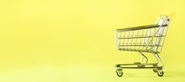 Alışveriş sepeti sarı zemin üzerine. Minimalizm tarzı. Yaratıcı tasarım. Uzay kopyalayın. Afiş. Süpermarkette alışveriş arabası. Satış, iskonto, shopaholism kavramı. Tüketici Derneği eğilim