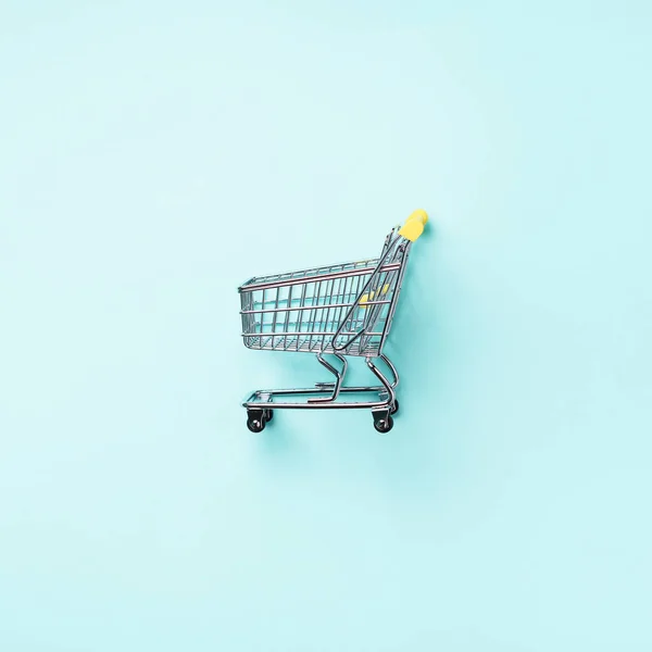 Shopping cart on blue background. Minimalism style. Square crop. Creative design. Top view with copy space. Shop trolley at supermarket. Sale, discount, shopaholism concept. Consumer society trend