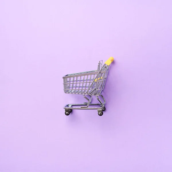 Shopping cart on purple background. Minimalism style. Square crop. Creative design. Top view with copy space. Shop trolley at supermarket. Sale, discount, shopaholism concept. Consumer society trend