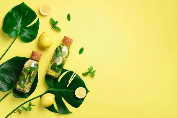 Garrafa de água de desintoxicação com folhas de hortelã, limão e monstera tropical sobre fundo amarelo. Deitado. Limonada cítrica. Fruta de verão água infundida. Vista superior com espaço de cópia . — Fotografia de Stock