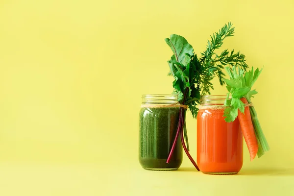 Здоровые органические зеленые и оранжевые коктейли на желтом фоне. Детоксикационные напитки в стеклянной банке из овощей - морковь, сельдерей, свекловичная зелень и топы. Принято. Концепция летней еды — стоковое фото