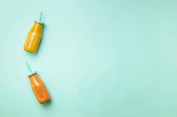 Fresh orange, banana, pineapple, mango smoothies and juicy fruits on blue background. Detox summer drink. Vegetarian concept. Top view, flat lay, copy space.