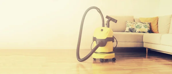 Cleaning service concept. Banner. Yellow vacuum cleaner, sofa on light background with copy space.