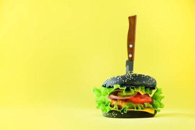 Fast food kavramı. Sarı zemin üzerine bıçakla sulu siyah burger. Yemek götürün. Sağlıksız beslenme çerçeve kopya alanı ile.